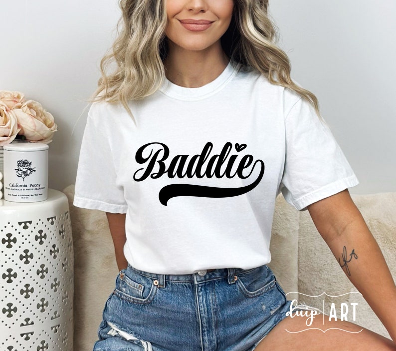K&ouml;nnte beinhalten: Wei&szlig;es T-Shirt mit dem Text "Baddie" in schwarzer Schrift mit einem kleinen Herzen &uuml;ber dem "e".