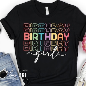 Puede incluir: Camiseta negra con el texto "Birthday girl" en colores arcoíris. El texto está apilado y contorneado en un estilo retro.