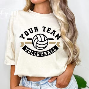 May include: A white t-shirt with a black and gold graphic design featuring a volleyball and the text "Your Team Volleyball".