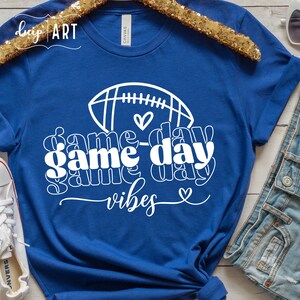 May include: A royal blue t-shirt with a white graphic design of a football and the text "game day vibes" with hearts.