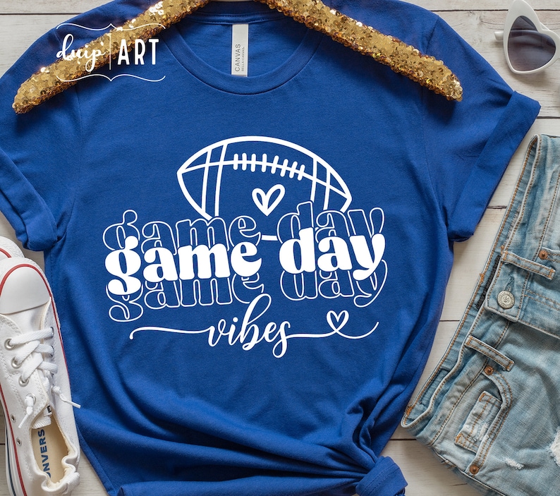 May include: A royal blue t-shirt with a white graphic design of a football and the text "game day vibes" with hearts.