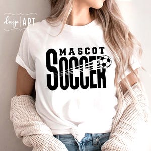 Pu&ograve; includere: Maglietta bianca con testo nero che recita "MASCOT SOCCER" e una grafica di un pallone da calcio bianco e nero.