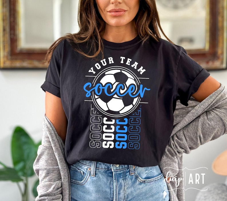 Pu&ograve; includere: Maglietta nera con una grafica di pallone da calcio bianco e il testo "Your Team Soccer" in blu e bianco. Il testo "Soccer" &egrave; ripetuto verticalmente in blu e bianco.
