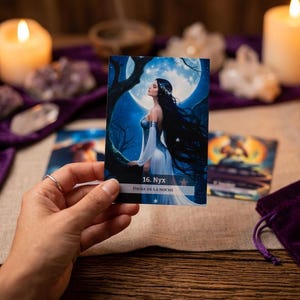 May include: A hand holds a tarot card depicting a woman with long black hair against a moonlit sky. The card is labeled "16. Nyx" and "Diosa de la Noche". The scene includes lit candles, crystals, and a purple velvet bag, suggesting a spiritual or divination theme.