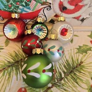 May include: A collection of Christmas ornaments in various colors, including red, green, and silver. Some ornaments feature decorative designs like leaves and berries. Each ornament has a gold-colored cap and a loop for hanging.