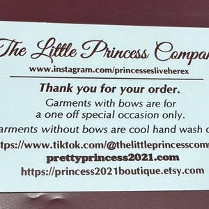 May include: A rectangular white card with dark brown text that reads The Little Princess Company, followed by social media links, a thank you message, and care instructions for garments with and without bows, including website addresses.