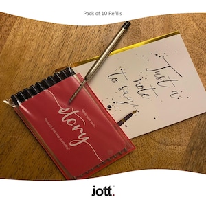 May include: A pack of 10 pen refills in a clear plastic sleeve with a red label that reads "story". A pen is placed on top of a white card with the text "Just a note to say". The brand "jott." is at the bottom.
