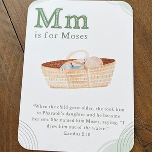 Peut inclure: Une carte d'alphabet illustr&eacute;e verte et blanche avec la lettre "M" et le mot "Mo&iuml;se". La carte repr&eacute;sente un b&eacute;b&eacute; dans un panier, avec le texte "Lorsque l'enfant a grandi, elle l'a emmen&eacute; &agrave; la fille de Pharaon et il est devenu son fils. Elle l'a appel&eacute; Mo&iuml;se, en disant : "Je l'ai tir&eacute; de l'eau." Exode 2:10"