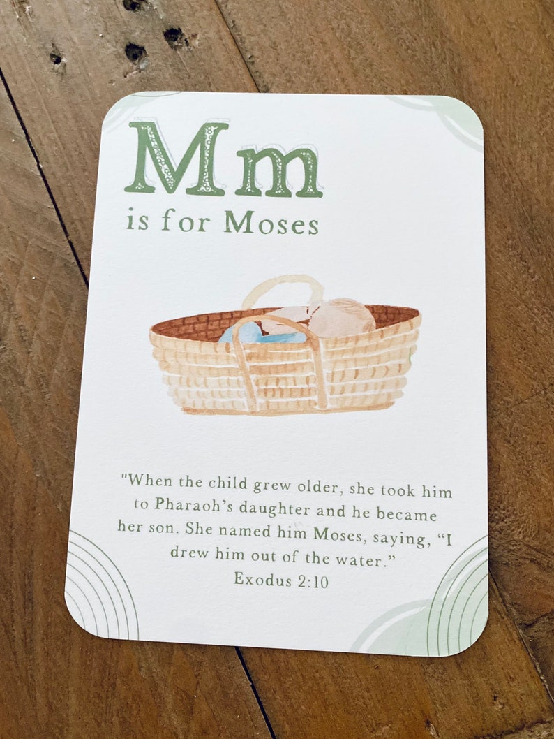 Peut inclure: Une carte d'alphabet illustr&eacute;e verte et blanche avec la lettre "M" et le mot "Mo&iuml;se". La carte repr&eacute;sente un b&eacute;b&eacute; dans un panier, avec le texte "Lorsque l'enfant a grandi, elle l'a emmen&eacute; &agrave; la fille de Pharaon et il est devenu son fils. Elle l'a appel&eacute; Mo&iuml;se, en disant : "Je l'ai tir&eacute; de l'eau." Exode 2:10"