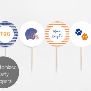 Puede incluir: Cuatro adornos circulares blancos para fiestas sobre palitos de madera. Los diseños incluyen círculos a rayas azules y naranjas con las palabras "TIGERS" y "War Eagle", un casco de fútbol azul e huellas de patas. Un círculo gris debajo dice "Customized Party Toppers!"