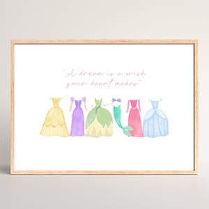 May include: Watercolor print in a wooden frame featuring five colorful dresses and a mermaid tail. The text "A dream is a wish your heart makes" is written above the dresses. The dresses are yellow, purple, green, pink, and blue.