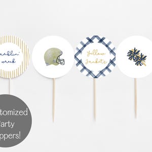May include: Four white cupcake toppers with football-themed designs. One has the text "Ramblin' Wreck", another a football helmet, a third says "Yellow Jackets", and the last shows pom-poms. Each topper is on a wooden stick.