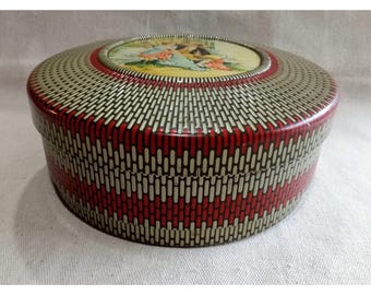 May include: A round, vintage tin box with a red and white striped pattern on the sides and a decorative lid. The lid features a colorful illustration of people in a garden setting. The tin has a shiny, reflective surface.