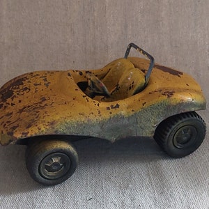 Puede incluir: Un coche de juguete amarillo con un exterior oxidado y ruedas negras. El coche tiene un diseño simple con un solo asiento y una barra antivuelco.