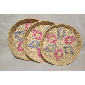 May include: Three round woven baskets with a floral design. The baskets are made of natural-colored straw and feature pink and blue accents. The floral pattern is centered on each basket.
