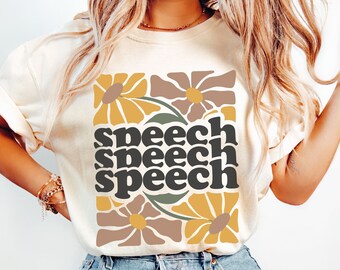 May include: Ivory-colored t-shirt with a floral design and the word "speech" repeated three times in a stacked format. The flowers are in shades of brown, yellow, and green. The shirt is made of a soft material.