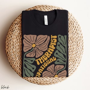 May include: Black t-shirt with a floral design and the text "Occupational Therapist" in yellow.