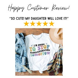 May include: White t-shirt with a colorful graphic that says "I'm going to stop procrastinating tomorrow". The shirt is laid out on a wooden surface with a denim jacket, a straw hat, and a white beaded necklace.