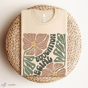 May include: A soft cream coloured t-shirt with a graphic design featuring stylised flowers and the text "Education Girl".