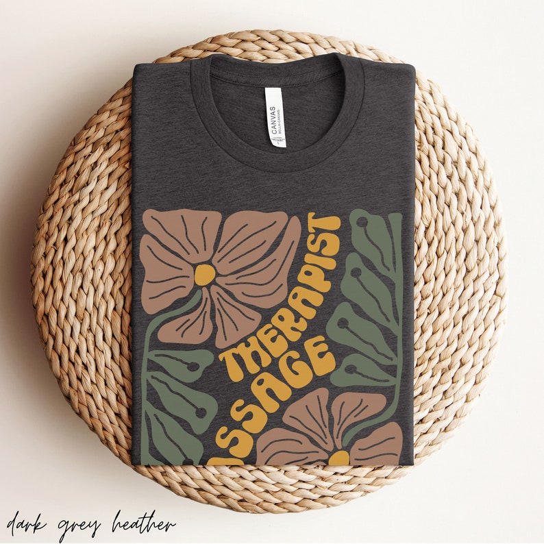 May include: Dark grey heather t-shirt with a floral design and the text "Massage Therapist" in a retro font.