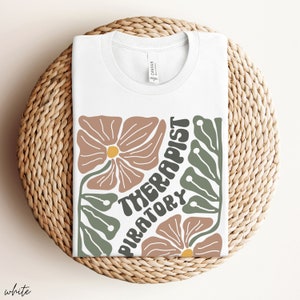 May include: White t-shirt with a floral design and the text "Respiratory Therapist" in a retro font.