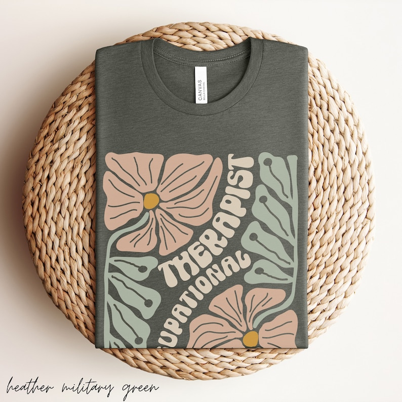 May include: A heather military green t-shirt with a floral design and the text "Occupational Therapist" in a retro font.