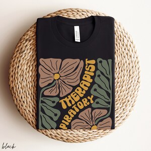 May include: Black t-shirt with a floral design and the text "Respiratory Therapist" in yellow.