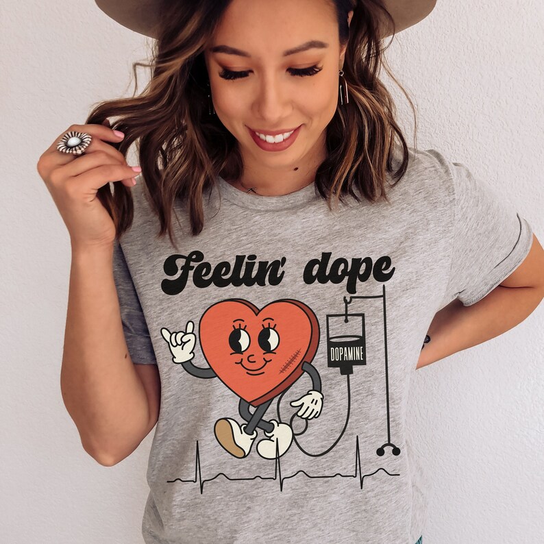May include: Gray t-shirt with a cartoon heart graphic and the text "Feelin' dope". The heart is connected to an IV bag labeled "Dopamine".