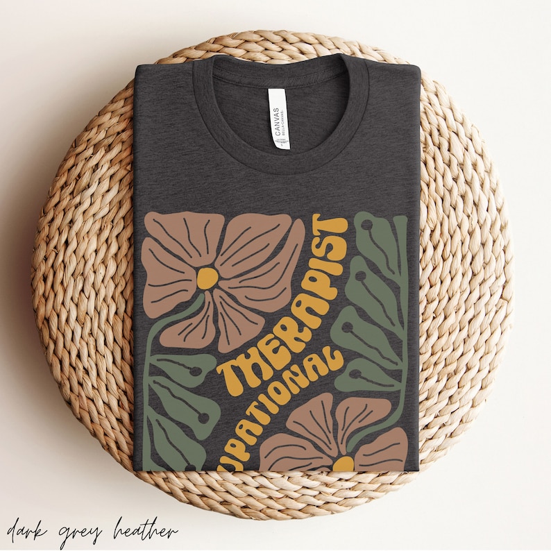 May include: Dark grey heather t-shirt with a floral design and the text "Occupational Therapist" in yellow.