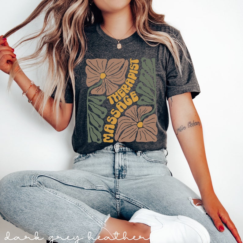 May include: A dark grey heather t-shirt with a floral design and the text "Massage Therapist" in yellow and orange letters.