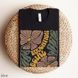 May include: Black t-shirt with a graphic design featuring stylised flowers and the text "Equal Education".