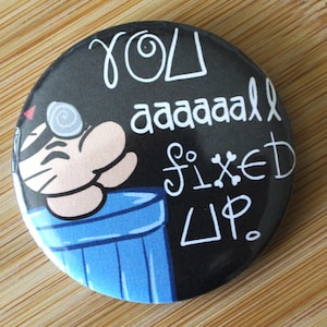Può includere: Bottone rotondo nero con testo bianco che recita "You aaaaaaall fixed up." Il bottone presenta un personaggio dei cartoni animati e un bidone della spazzatura blu. Lo sfondo è un legno marrone chiaro.