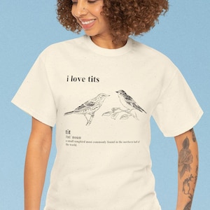 May include: Cream-colored t-shirt with the text "i love tits" above a drawing of two birds. Below the birds is the definition of the word "tit". The shirt is worn by a person.
