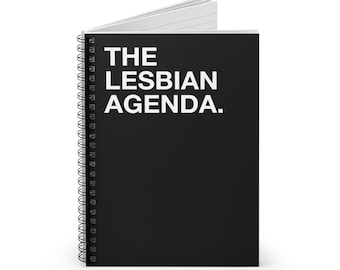 以下が含まれることがあります： 「THE LESBIAN AGENDA.」の白文字がプリントされた黒いスパイラルノート。ノートは開かれており、白い罫線入りのページが見える。スパイラルバインディングはシルバーです。