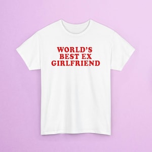 Könnte beinhalten: Weißes T-Shirt mit dem roten Text "WORLD'S BEST EX GIRLFRIEND". Das Shirt hat kurze Ärmel und einen Rundhalsausschnitt. Der Text ist mittig auf der Vorderseite des Shirts platziert.