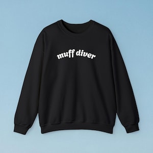 May include: Black crewneck sweatshirt with the text "muff diver" in white, curved, cursive font. The sweatshirt has long sleeves and a ribbed neckline, cuffs, and hem. The background is a light blue.