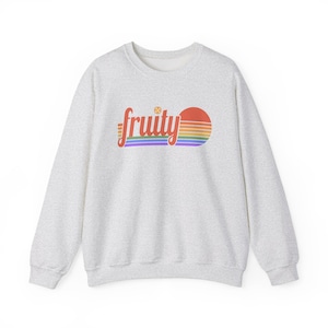 May include: A light gray sweatshirt with the word "fruity" in a rainbow-colored script across the chest. The word is above a rainbow-striped design with a red sun. The sweatshirt has a crew neck and long sleeves.