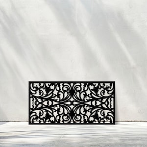 May include: Black decorative panel with an intricate, symmetrical floral design. The panel is rectangular and stands against a white wall, casting shadows. The design features swirling leaves and curves, suitable for home decor.