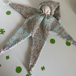 Op de afbeelding: Een gebreide babypop met een capuchon en lange benen. De pop is gemaakt van een veelkleurig garen in tinten groen, blauw, oranje en roze.