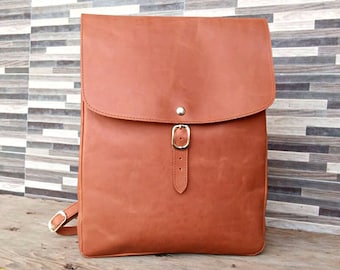 Puede incluir: Una mochila de cuero marrón con un cierre de hebilla simple y una solapa con un botón plateado. La mochila tiene un diseño sencillo y está hecha de cuero de alta calidad.