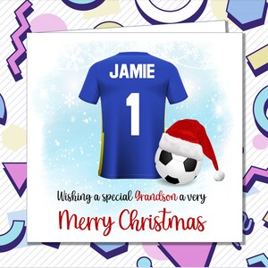May include: A blue football shirt with the name "JAMIE" and the number "1" on the back. A football with a Santa hat is in the foreground. The text "Wishing a special Grandson a very Merry Christmas" is below the shirt.