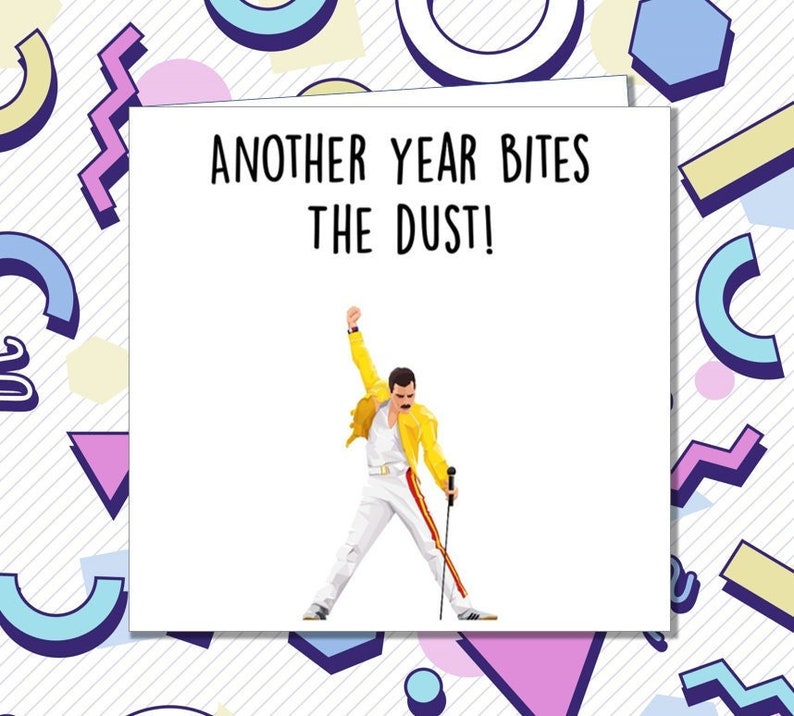 Op de afbeelding: Een witte kaart met de tekst "Another year bites the dust!" en een cartoon afbeelding van Freddie Mercury in een geel jack en een witte broek, die een microfoon vasthoudt.