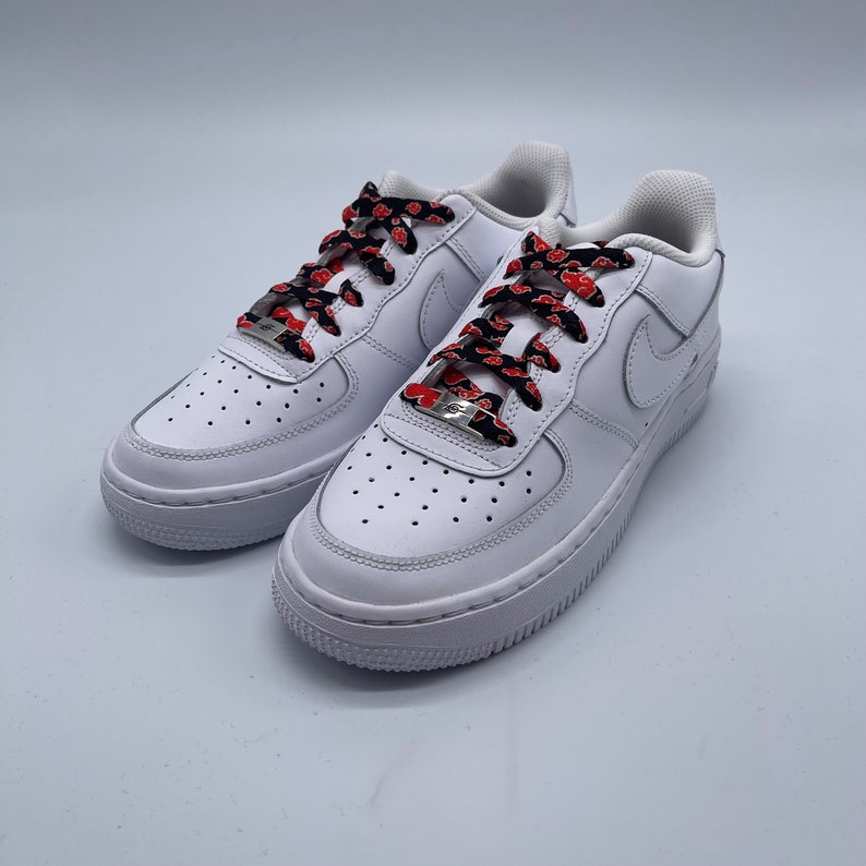 Puede incluir: Zapatillas bajas de cuero blanco con cordones de patr&oacute;n rojo y negro. Los cordones tienen un patr&oacute;n repetido de nubes rojas sobre un fondo negro.
