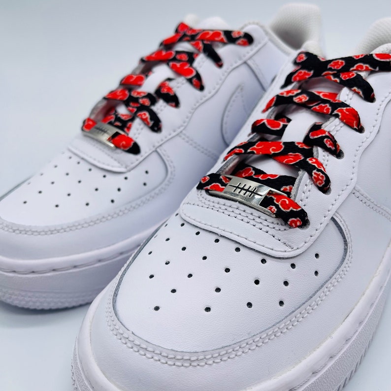 Puede incluir: Zapatillas blancas con cordones rojos y negros que presentan un patr&oacute;n repetido de nubes rojas sobre un fondo negro. Los cordones est&aacute;n atados con un cierre de cordones plateado con la palabra "HITH" grabada.
