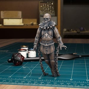 May include: A painted miniature of a skeletal figure wearing a chainmail shirt and a ruff collar. The figure is holding chains in its hands and is standing on a green cutting mat.