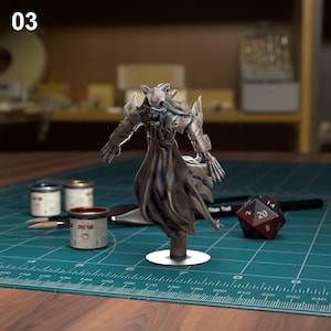 K&ouml;nnte beinhalten: Eine detaillierte Miniaturfigur einer skelettartigen Gestalt, die einen Kapuzenumhang tr&auml;gt. Die Figur ist in Graut&ouml;nen und Wei&szlig; bemalt und in einer dramatischen Pose dargestellt. Die Figur steht auf einem runden Sockel und ist von einer gr&uuml;nen Schneidematte umgeben.