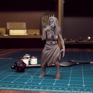 K&ouml;nnte beinhalten: Eine bemalte Miniaturfigur einer weiblichen Humanoiden mit spitzen Ohren, Z&auml;hnen und langen Haaren. Sie tr&auml;gt einen braunen Rock und ein &auml;rmelloses Oberteil. Die Figur steht auf einer gr&uuml;nen Oberfl&auml;che mit einem Lineal und Farbt&ouml;pfen.