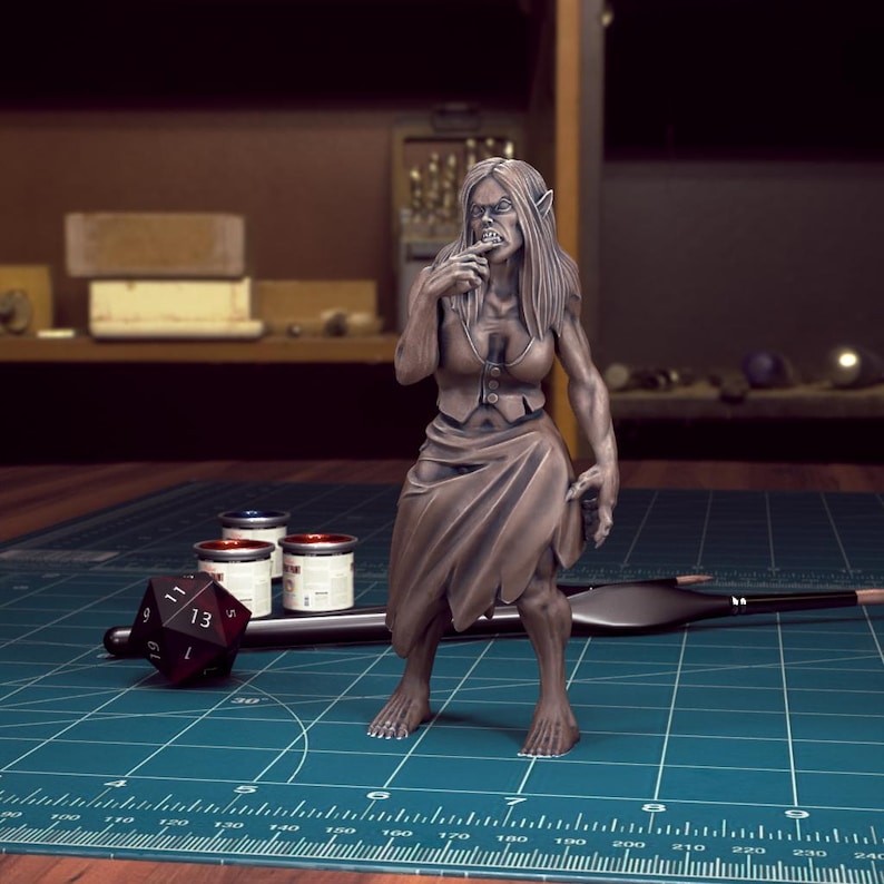 K&ouml;nnte beinhalten: Eine bemalte Miniaturfigur einer weiblichen Humanoiden mit spitzen Ohren, Z&auml;hnen und langen Haaren. Sie tr&auml;gt einen braunen Rock und ein &auml;rmelloses Oberteil. Die Figur steht auf einer gr&uuml;nen Oberfl&auml;che mit einem Lineal und Farbt&ouml;pfen.