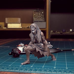 K&ouml;nnte beinhalten: Eine bemalte Miniaturfigur einer weiblichen Kreatur mit langen Haaren und scharfen Z&auml;hnen, in einer aggressiven, knurrenden Pose. Die Figur ist in Graut&ouml;nen und Braun bemalt, wobei Details der Gesichtsz&uuml;ge der Kreatur in Wei&szlig; hervorgehoben sind.