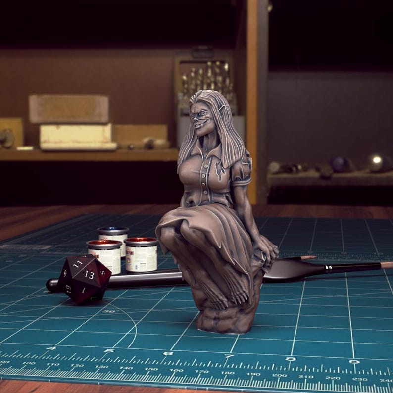 K&ouml;nnte beinhalten: Eine bemalte Miniaturfigur einer weiblichen Figur mit spitzen Ohren, die ein Kleid tr&auml;gt und auf einem Felsen sitzt. Die Figur ist in Bronzefarben bemalt.